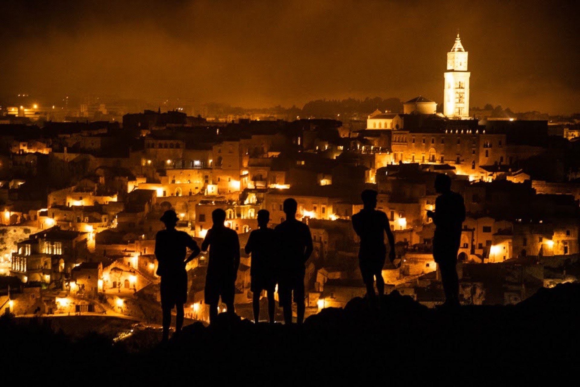 Silhouettes of people watching a glowing Italian hilltop city at night