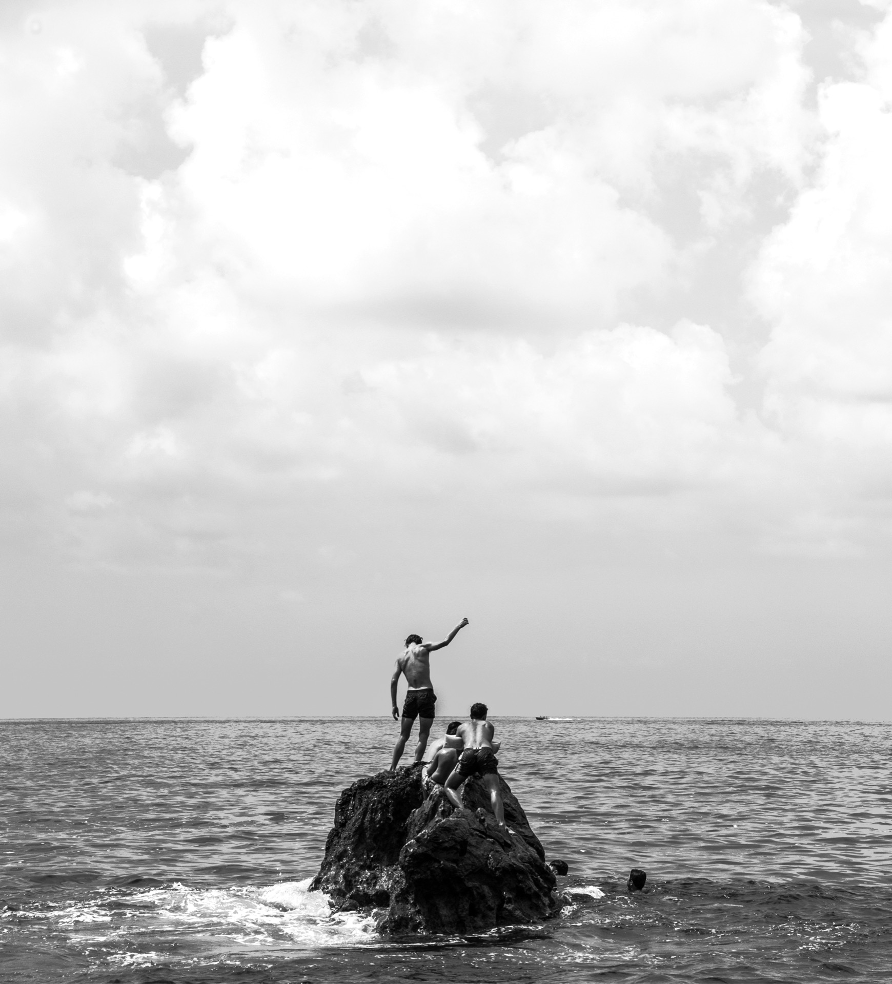 Boys on a sea rock, one raising a fist in victory, black and white