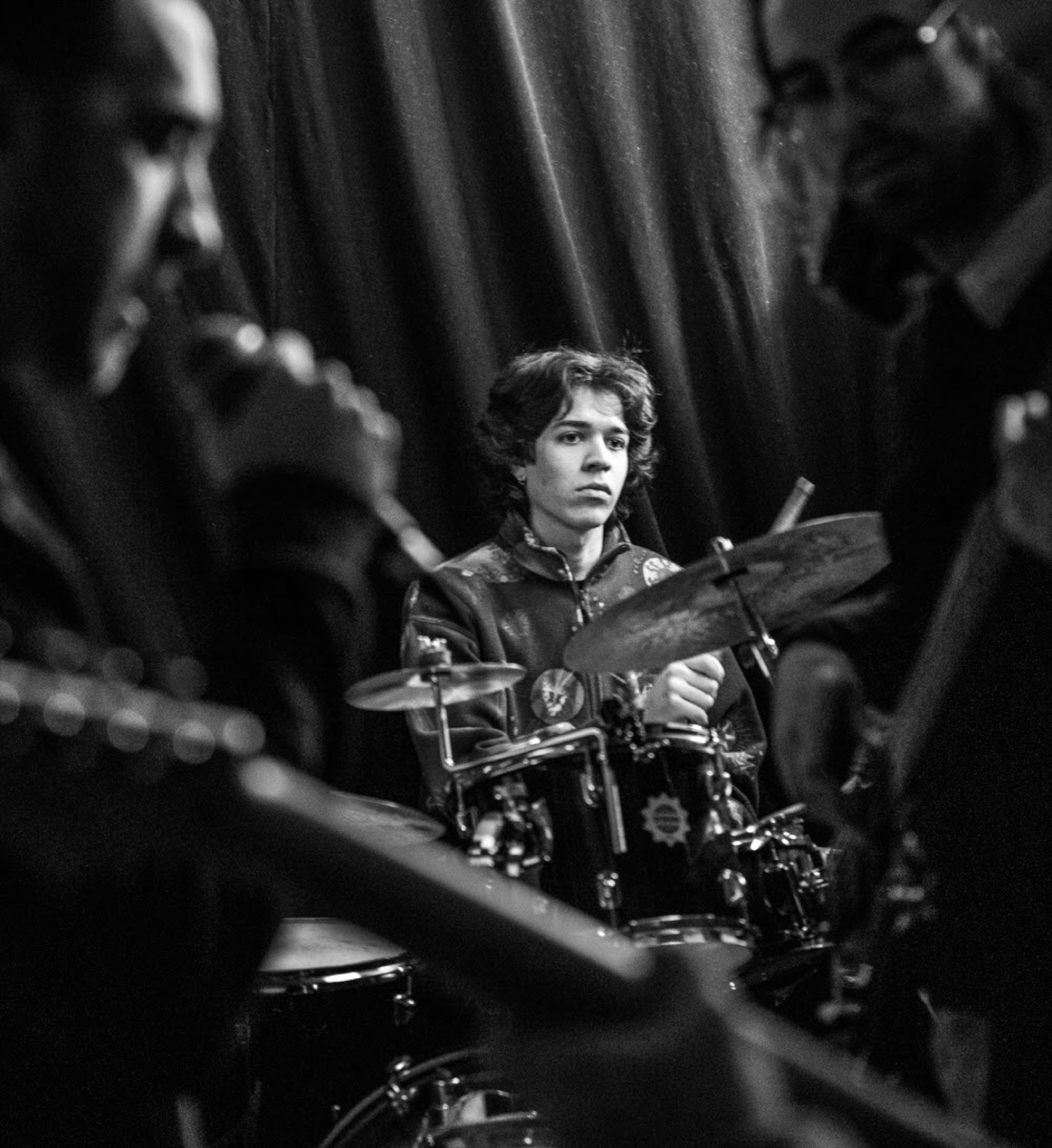 Young drummer seen through other musicians, black and white