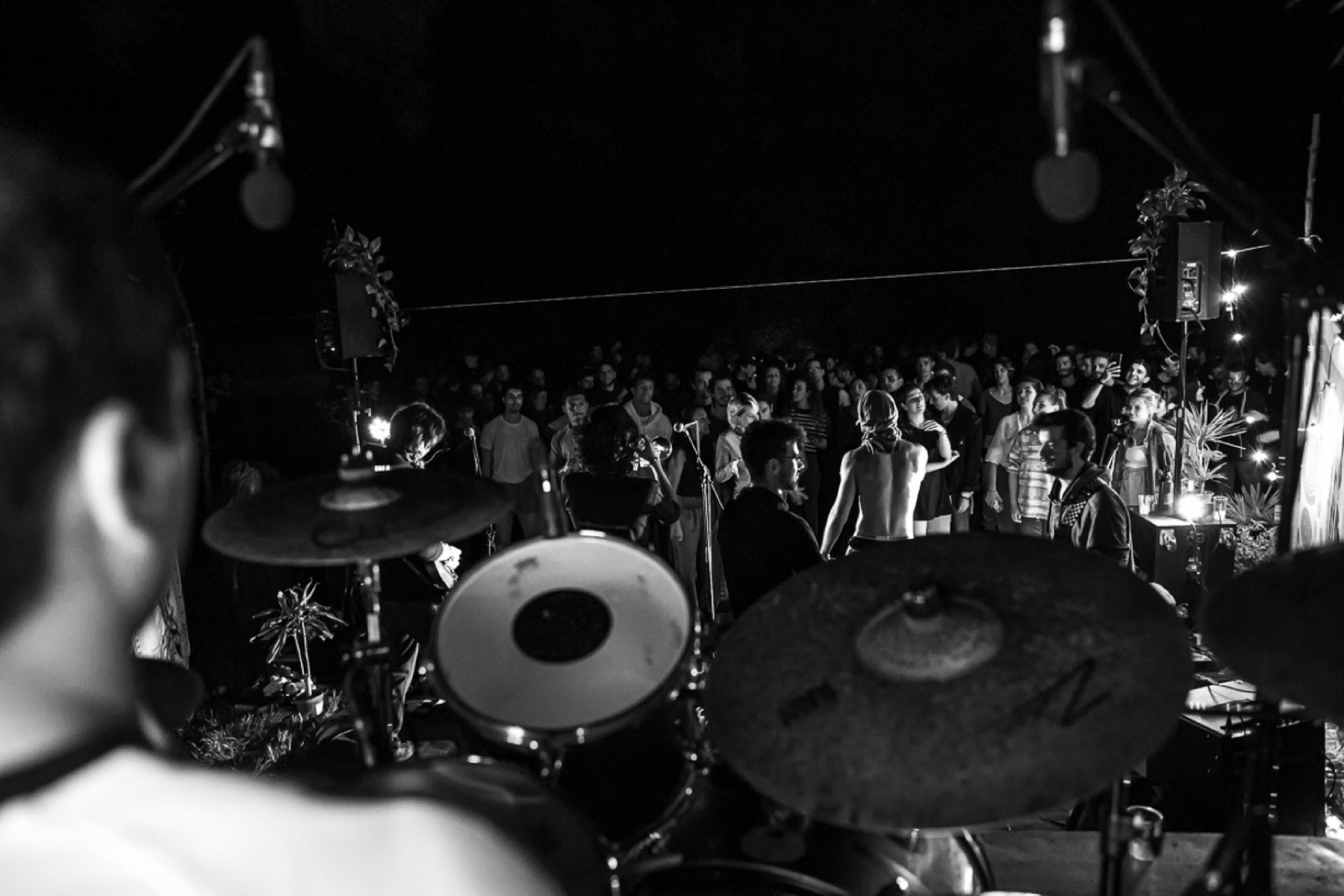 Concert seen from behind the drumkit, crowd in black and white
