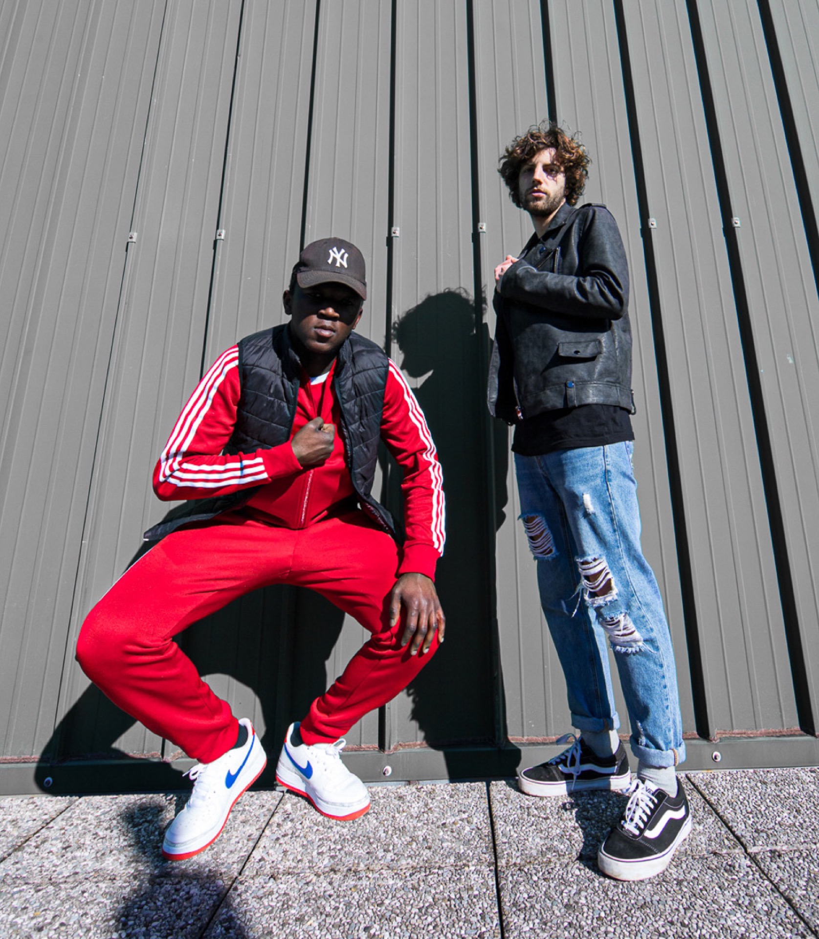 Two hip hop artists posing against corrugated metal