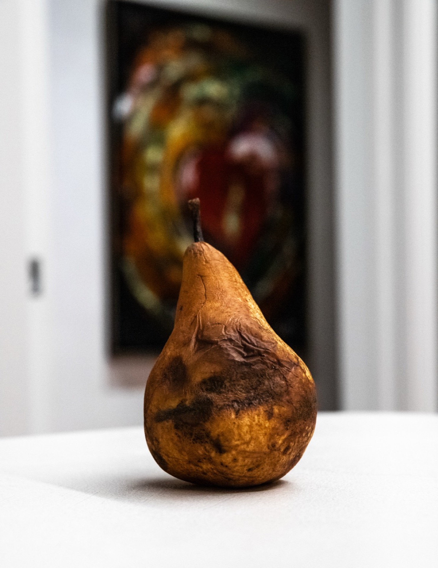 Aged pear on a white surface with colourful painting in background, macro